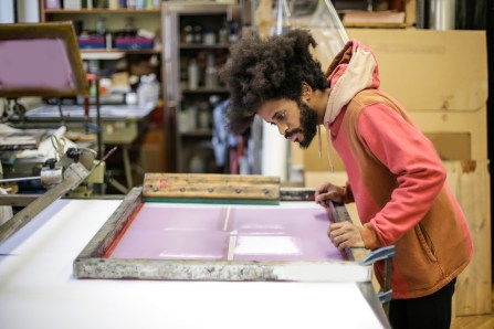 Canva - Creative young ethnic craftsman working with screen printing in workshop